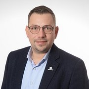In einem hellen Hintergrund posiert ein Mann mit Brille, der selbstbewusst und freundlich wirkt.