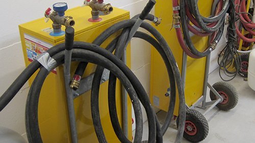 Zwei gelbe Geräte mit verschiedenen Anschlüssen und Schläuchen stehen nebeneinander, bereit für technische Anwendungen.