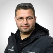 Ein Mann mit Brille und kurzem, dunklem Haar trägt eine schwarze Jacke und schaut direkt in die Kamera.