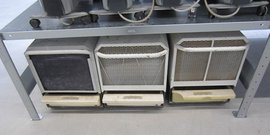 Ein Metallregal trägt drei Geräte mit Gitterstrukturen, die in verschiedenen Zuständen der Abnutzung sind.