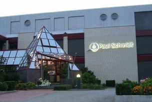 Das moderne Gebäude mit einer gläsernen Pyramide und dem Schriftzug 'Paul Schmidt' ist von bunten Blumen umgeben.