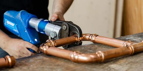 Die Hände eines Handwerkers halten ein Werkzeug, das Kupferrohre zusammenfügt, um eine stabile Verbindung zu schaffen.