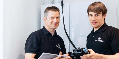 Die beiden Männer in schwarzen Poloshirts präsentieren stolz ihre Ausrüstung in einer modernen Umgebung.