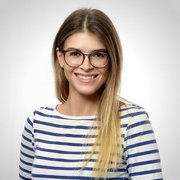 Eine junge Frau mit langen, blonden Haaren und Brille lächelt freundlich in die Kamera, gekleidet in ein gestreiftes Oberteil.