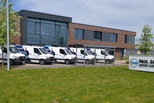 Vor einem modernen Gebäude stehen mehrere weiße Lieferwagen mit Werbung für Heizungs- und Sanitärdienstleistungen.