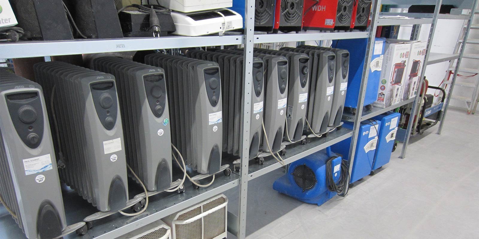 Eine Reihe von grauen Heizgeräten steht ordentlich auf Regalen, umgeben von verschiedenen elektrischen Geräten und Zubehör.