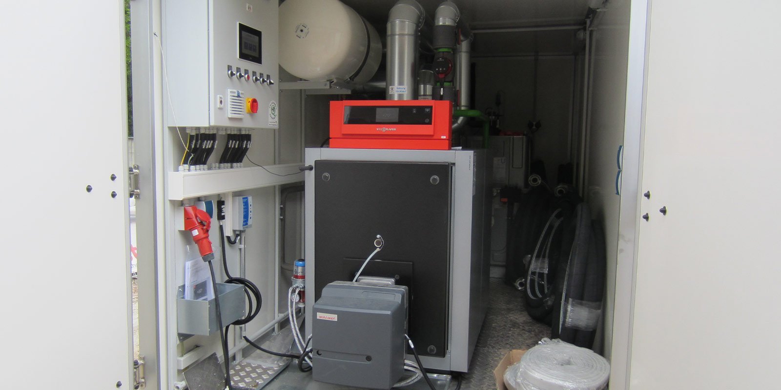 Ein technischer Raum mit einer großen Heizungsanlage, die von Rohren und Kabeln umgeben ist, zeigt moderne Ausrüstung.