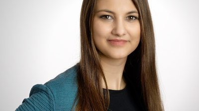 Eine junge Frau mit langen, glatten Haaren lächelt freundlich in die Kamera, während sie einen blauen Cardigan trägt.