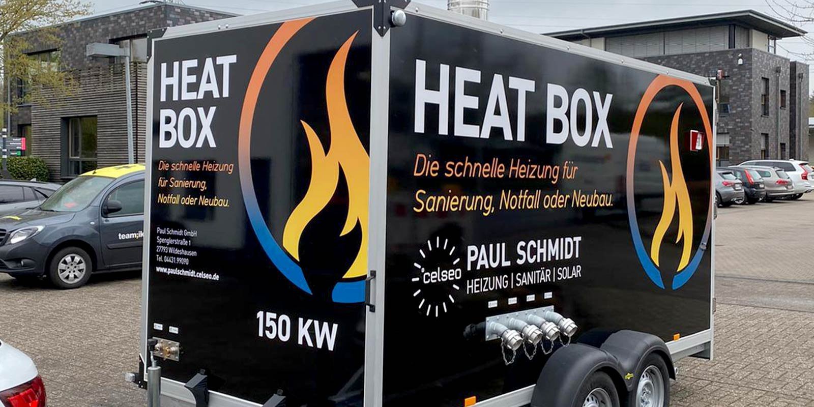 Ein Heizungsanhänger mit der Aufschrift 'HEAT BOX' steht auf einem Parkplatz, umgeben von mehreren Autos.