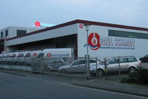 Das Gebäude von Paul Schmidt ist modern und gut beleuchtet, mit mehreren Fahrzeugen, die vor dem Eingang geparkt sind.
