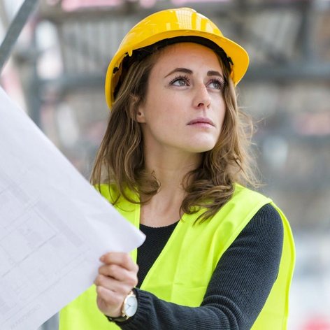 Eine Frau mit Bauhelm hält eine Zeichnung auf einer Baustelle