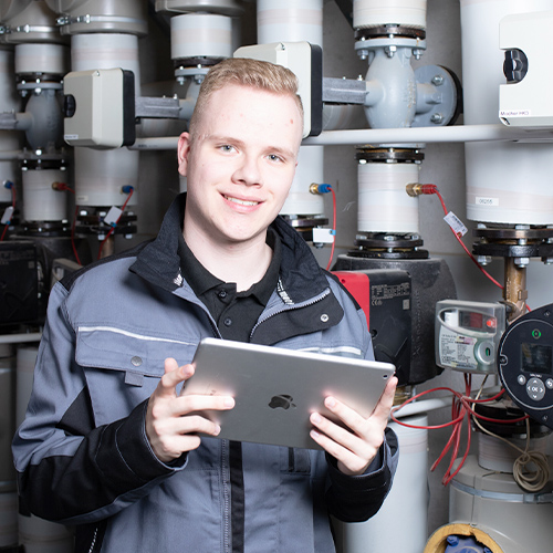 Ein Anlagenmechaniker steht mit seinem Firmentablet vor einer modernen Heizung